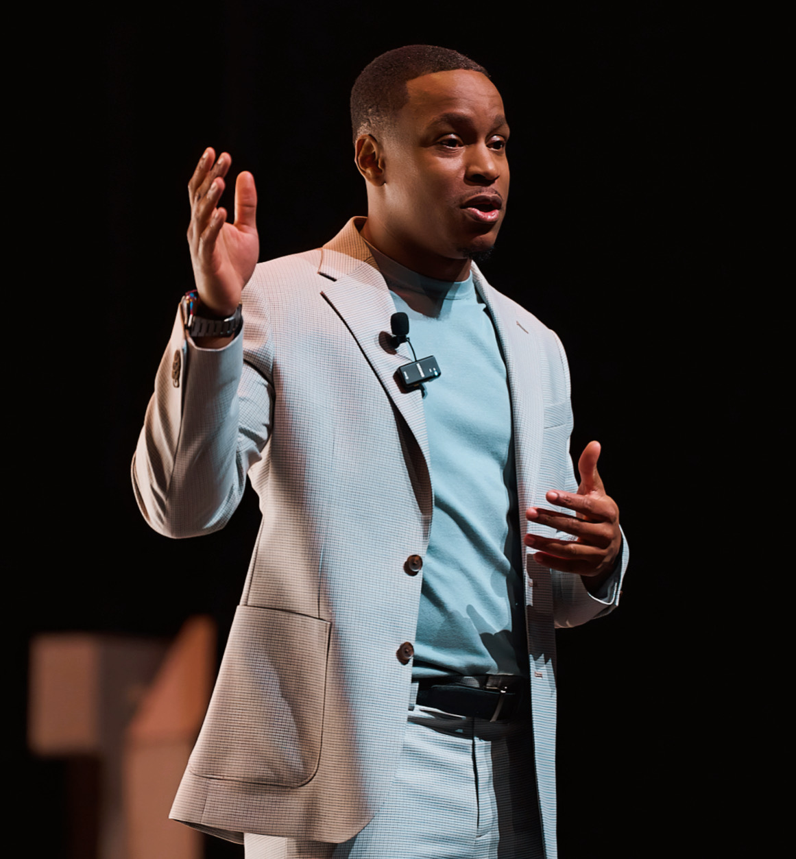 Jamyle Cannon mid-speech in a light suit, gesturing with both hands on stage