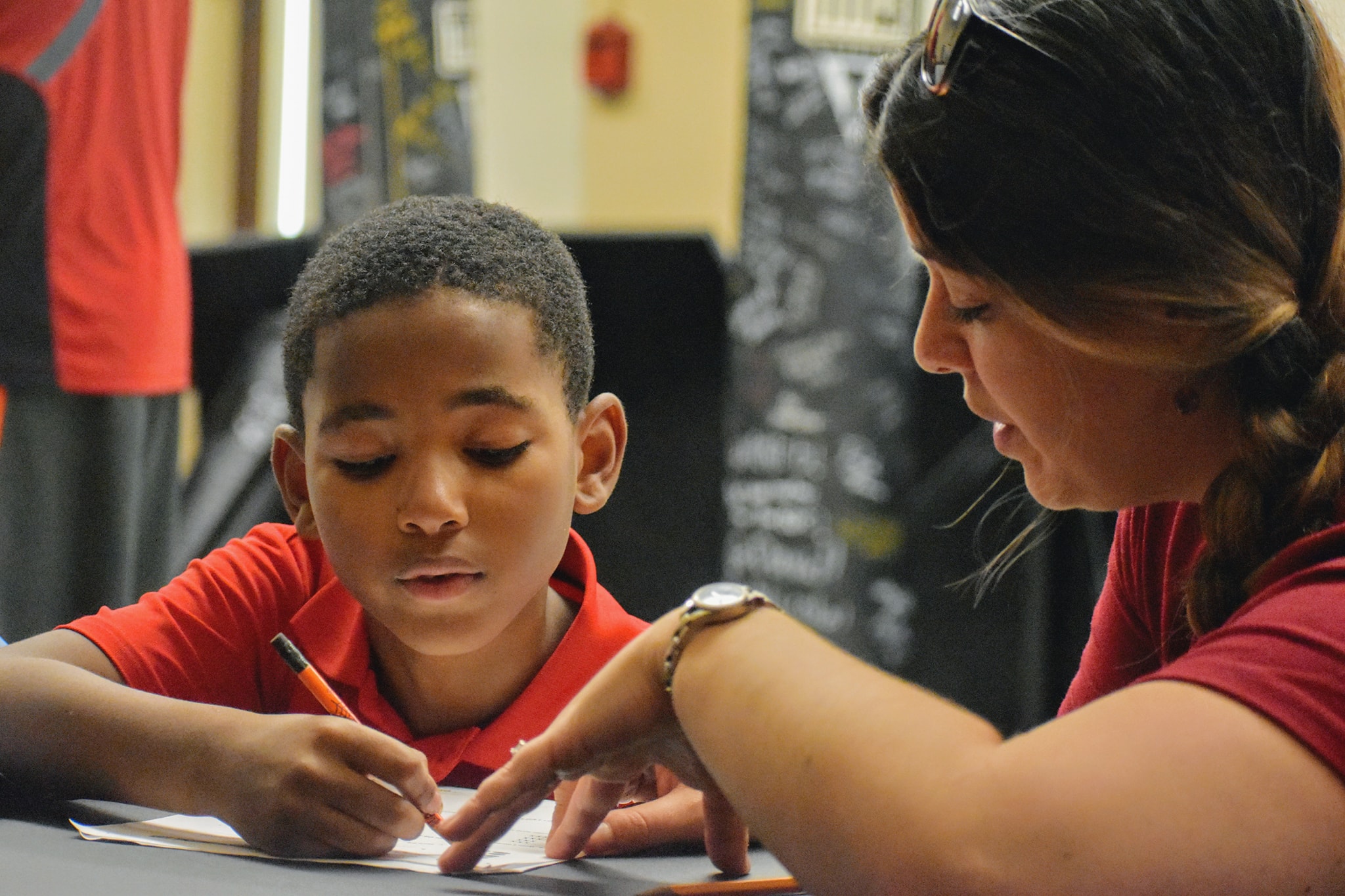 A mentor sits beside a young student helping them write
